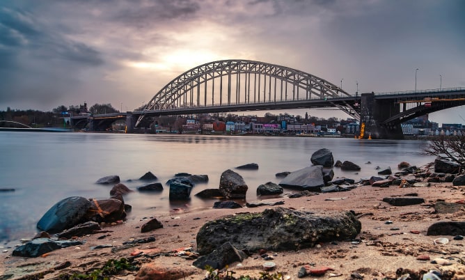 Brug over rivier bij zonsondergang met stenen strand.